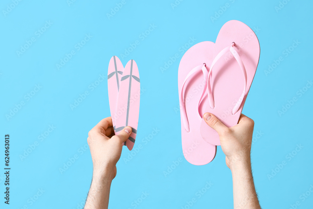 Male hands with flip flops and mini surfboards on blue background