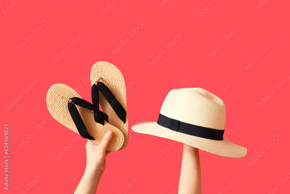 Female hands with wicker hat and flip flops on red background