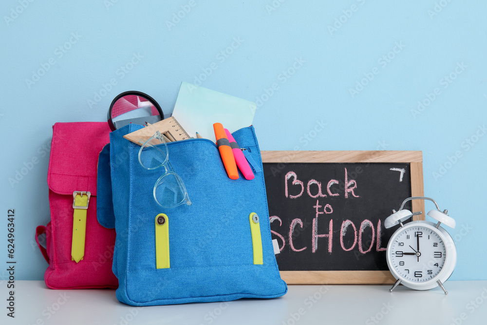 Colorful school backpacks, stationery and blackboard with text BACK TO SCHOOL on white table near bl