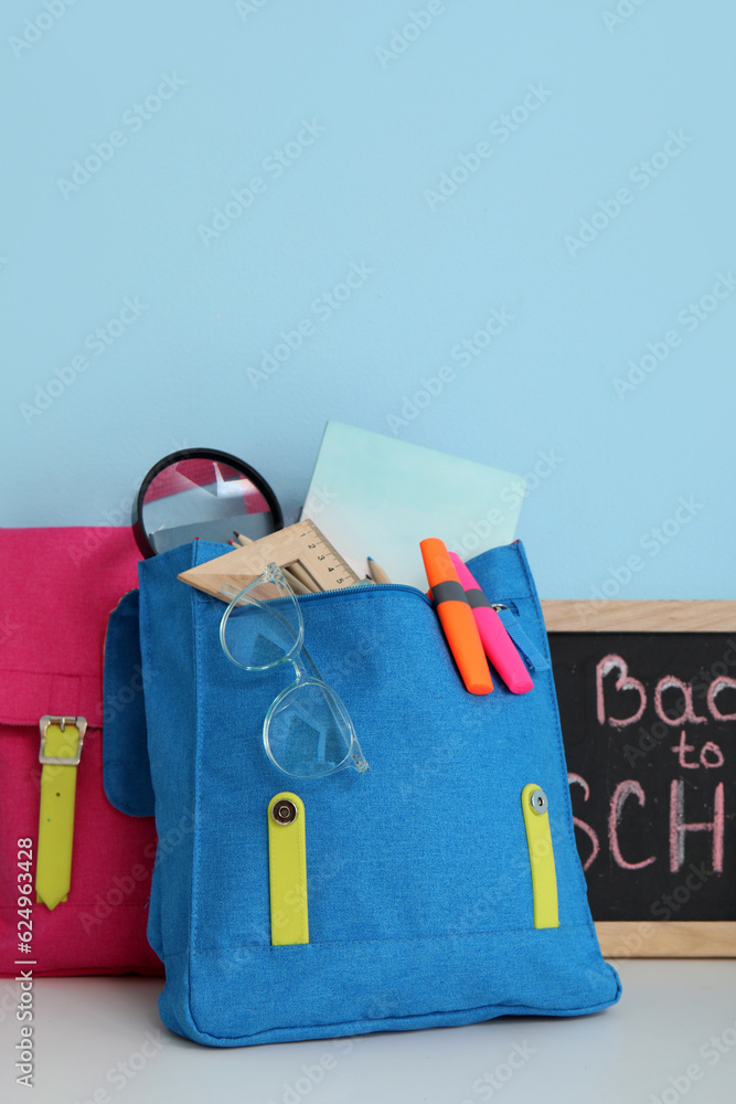 Colorful school backpacks, stationery and blackboard with text BACK TO SCHOOL on white table near bl