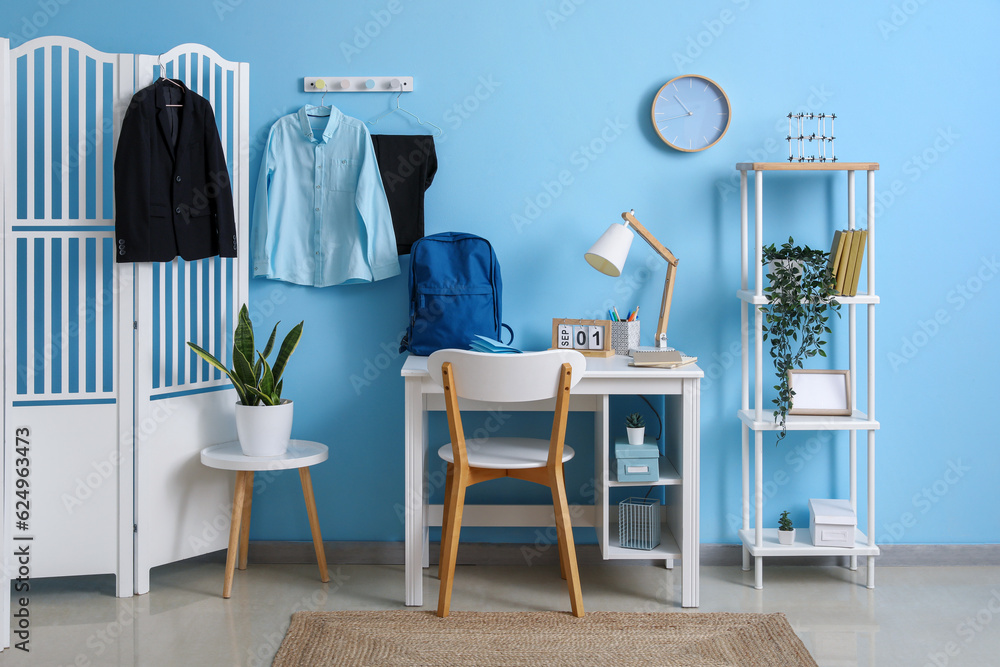 Interior of workplace with desk, shelving unit, folding screen, clock and stylish school uniform han