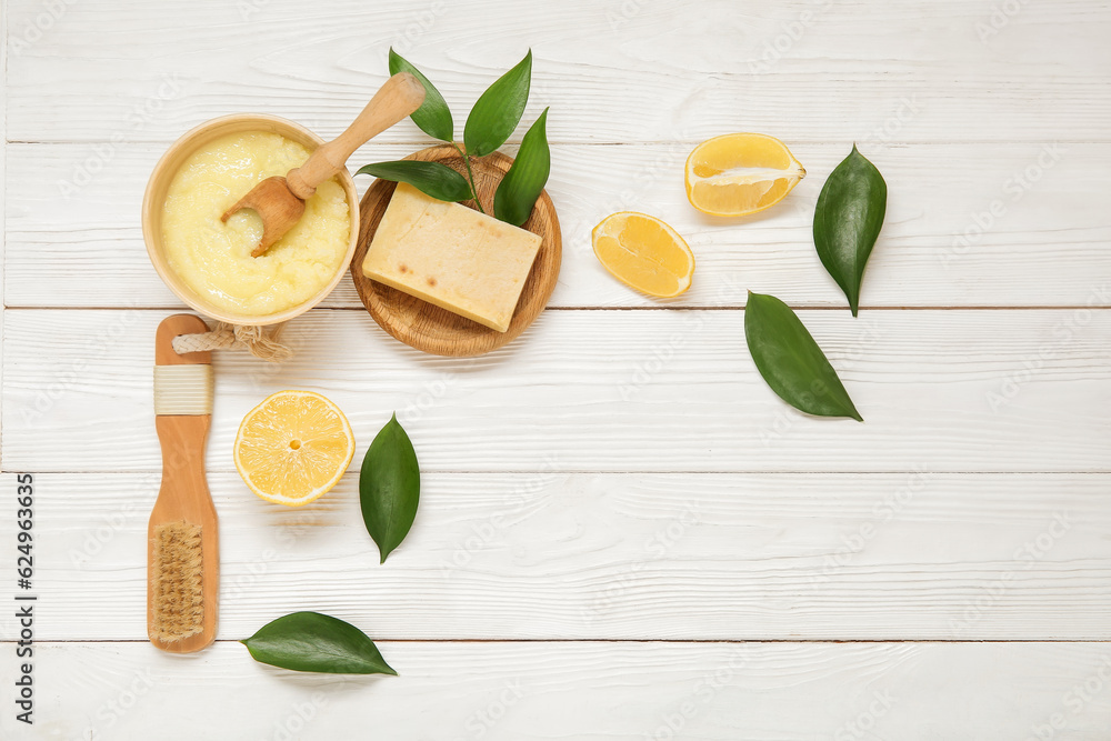 Bowl of lemon body scrub with massage brush and soap on white wooden background