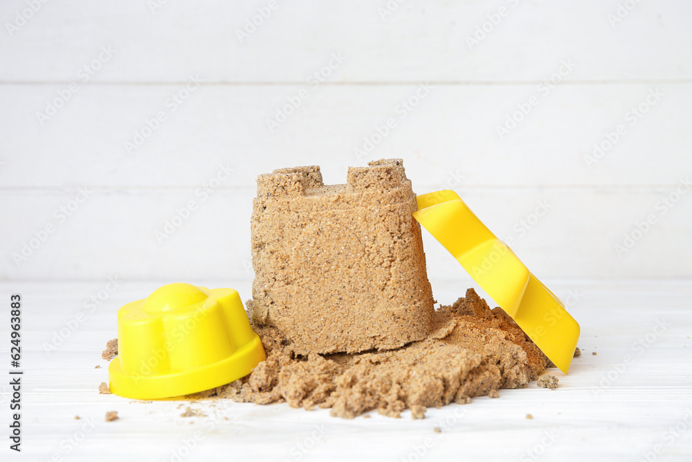 Castle made of sand with beach toys on white wooden background