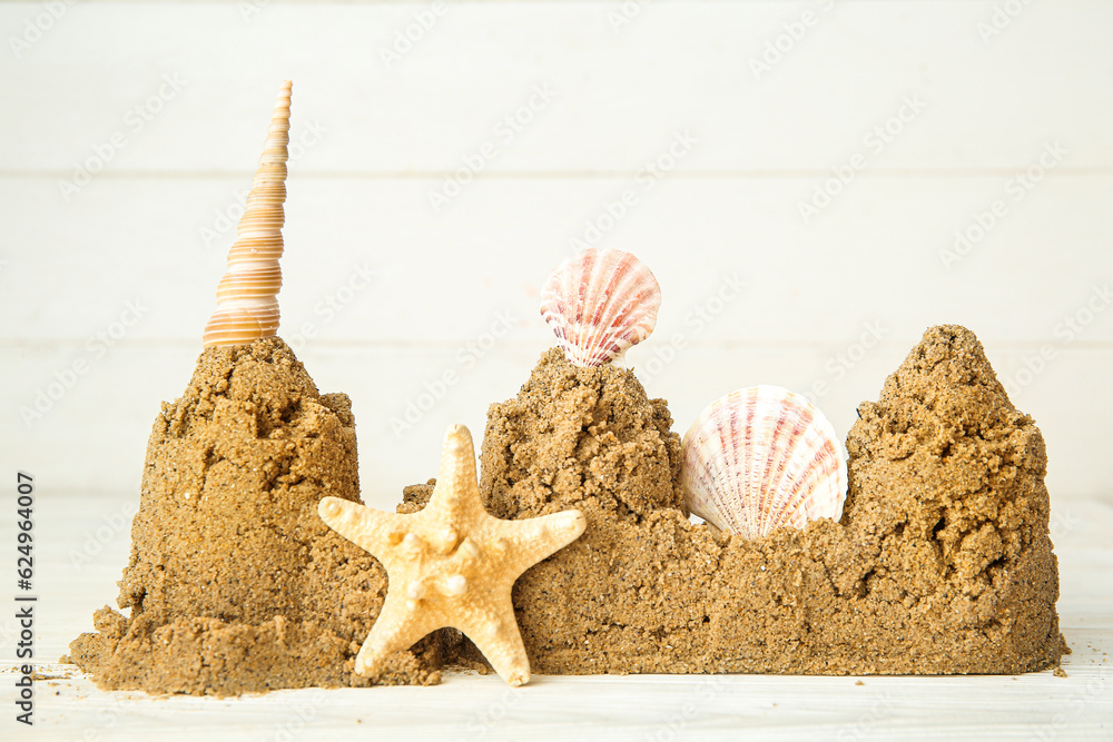 Castle made of sand with starfish and seashells on white wooden background