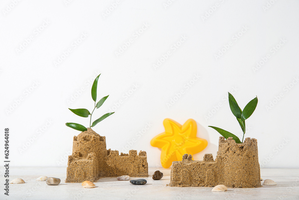 Castle made of sand with beach toy and plant branch on white background