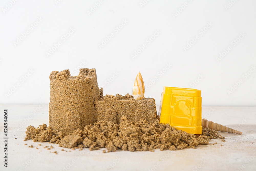 Castle made of sand with beach toy and seashell on white background