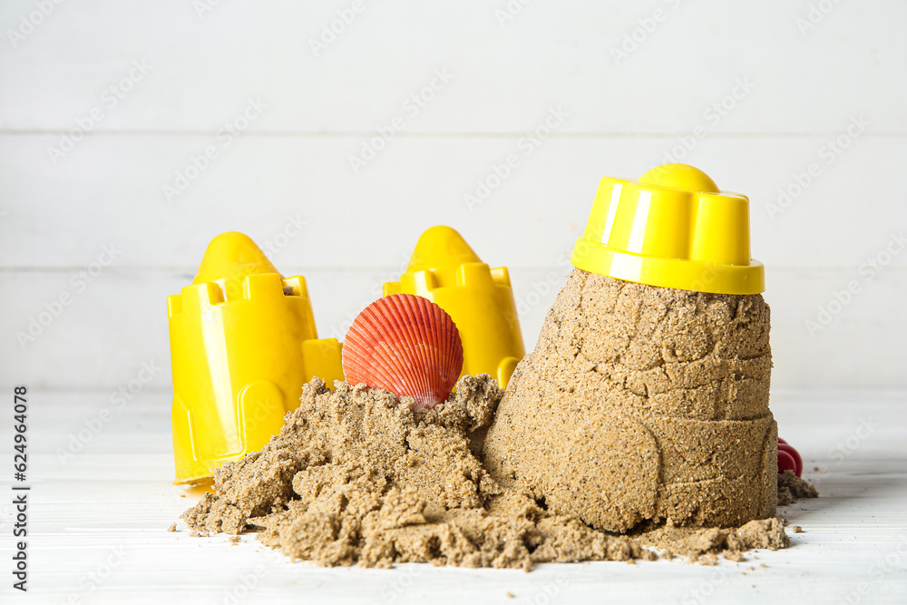 Castle made of sand with beach toys and seashell on white wooden background