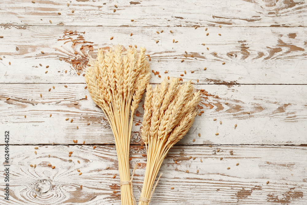 Bundle of wheat ears and grains on white wooden table