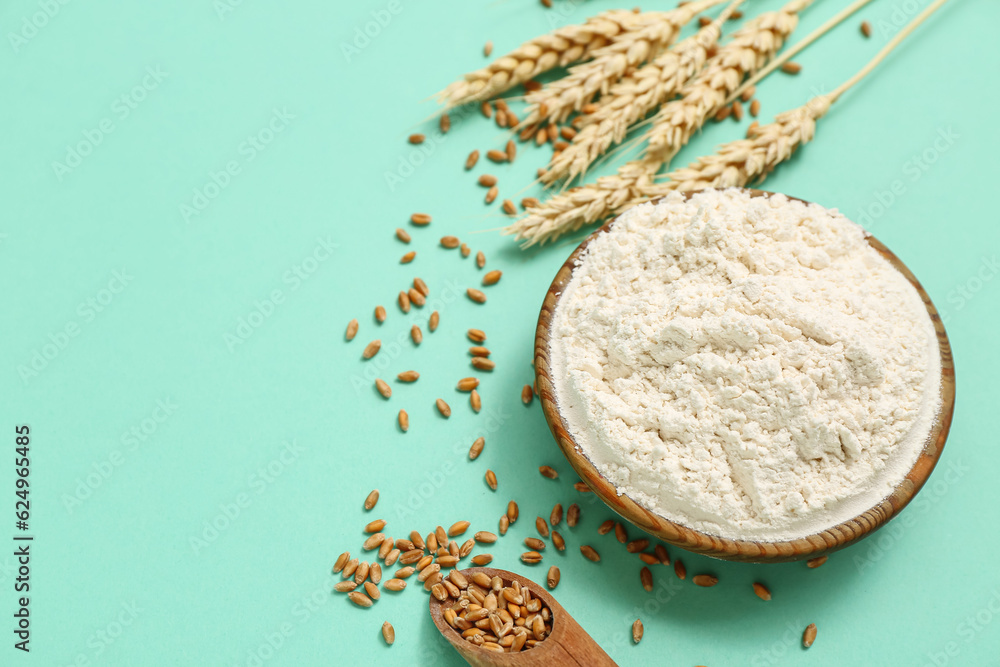 Bowl with wheat flour, scoop and spikelets on turquoise background