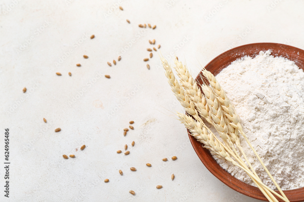 Bowl with wheat flour and spikelets on white table, closeup