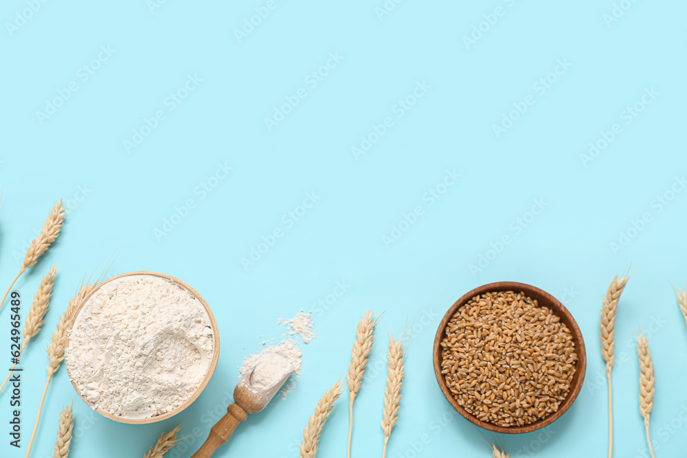 Bowls with wheat flour, grains and spikelets on blue background