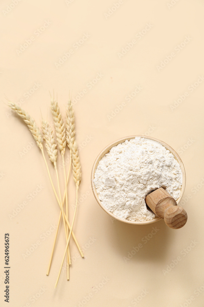 Bowl with wheat flour and scoop on beige background