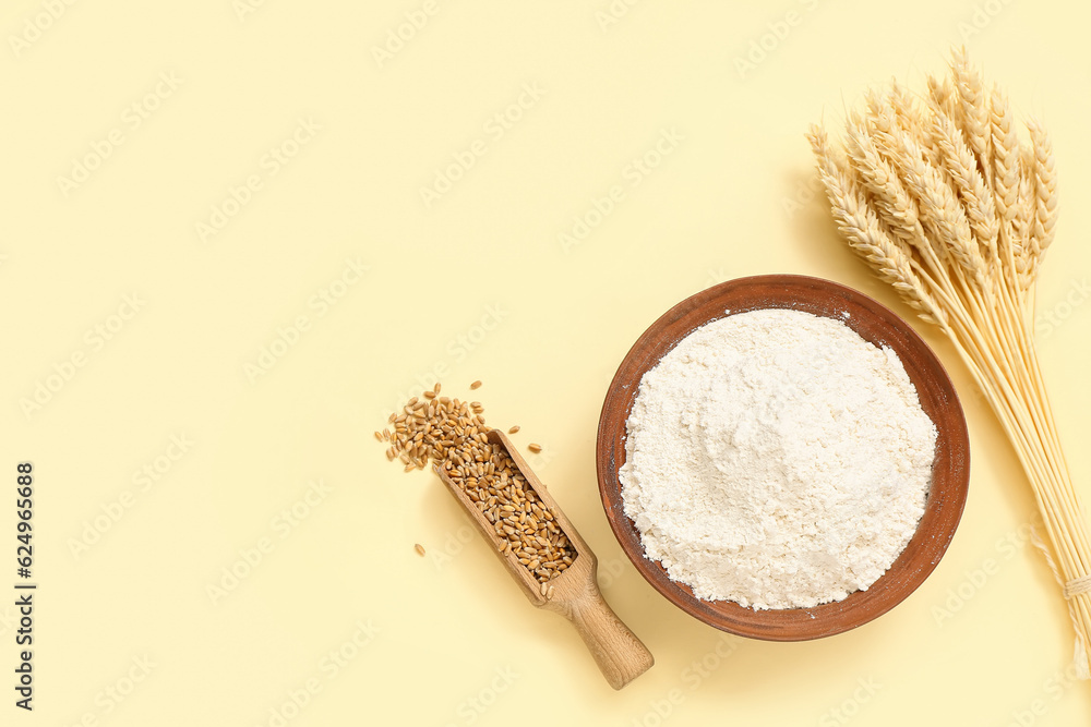 Bowl with wheat flour, scoop and spikelets on yellow background