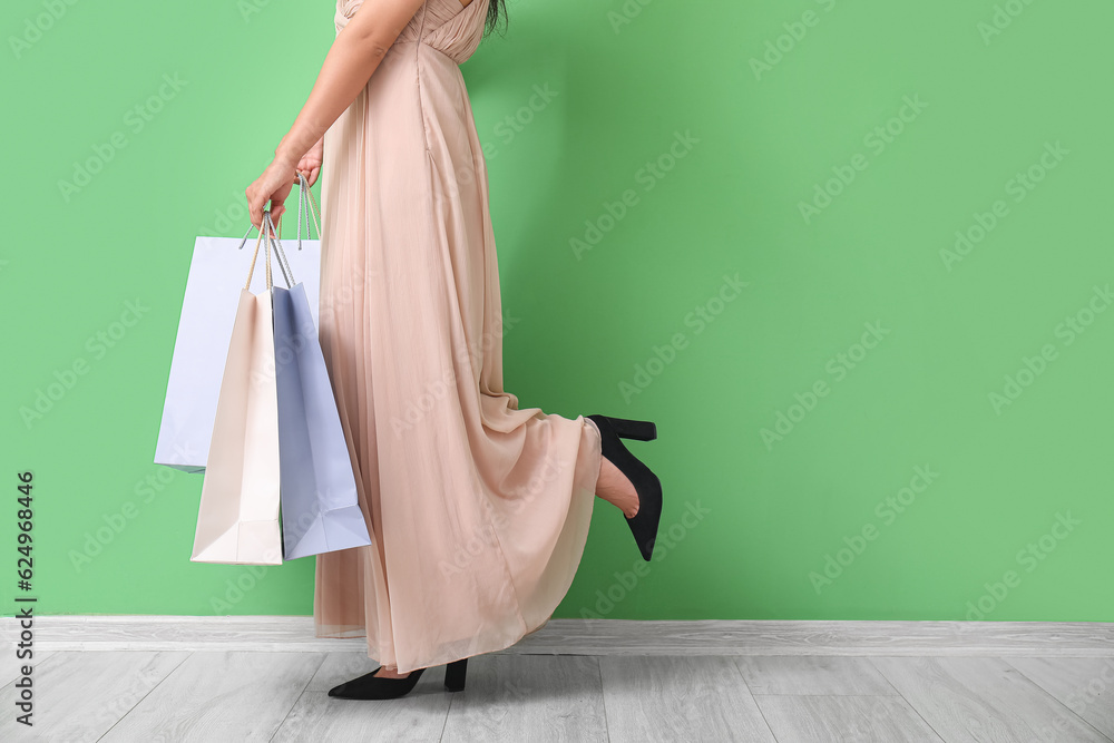 Beautiful young woman with shopping bags near green wall