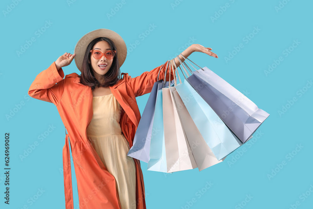 Happy beautiful young Asian woman with shopping bags on blue background