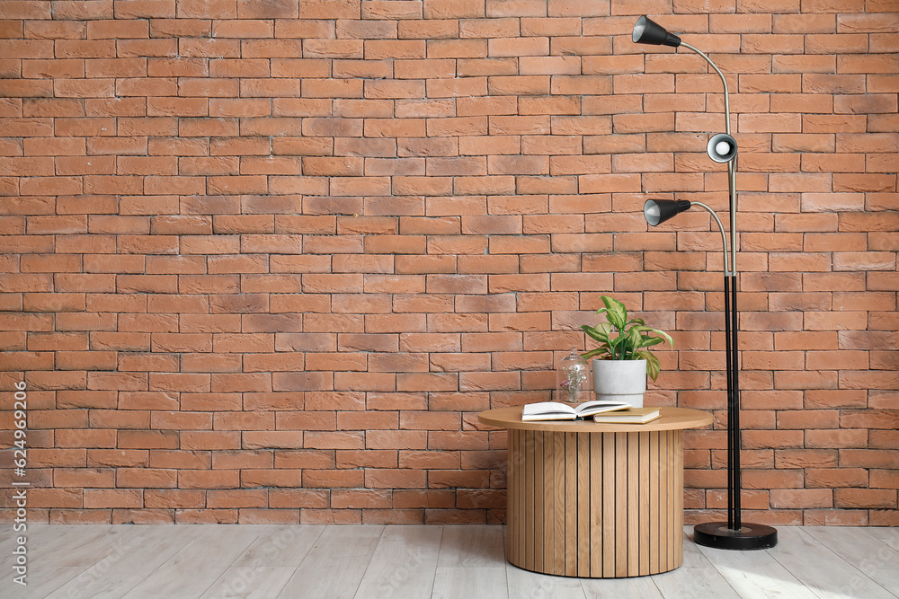 Wooden coffee table with books and home decor in room near brick wall