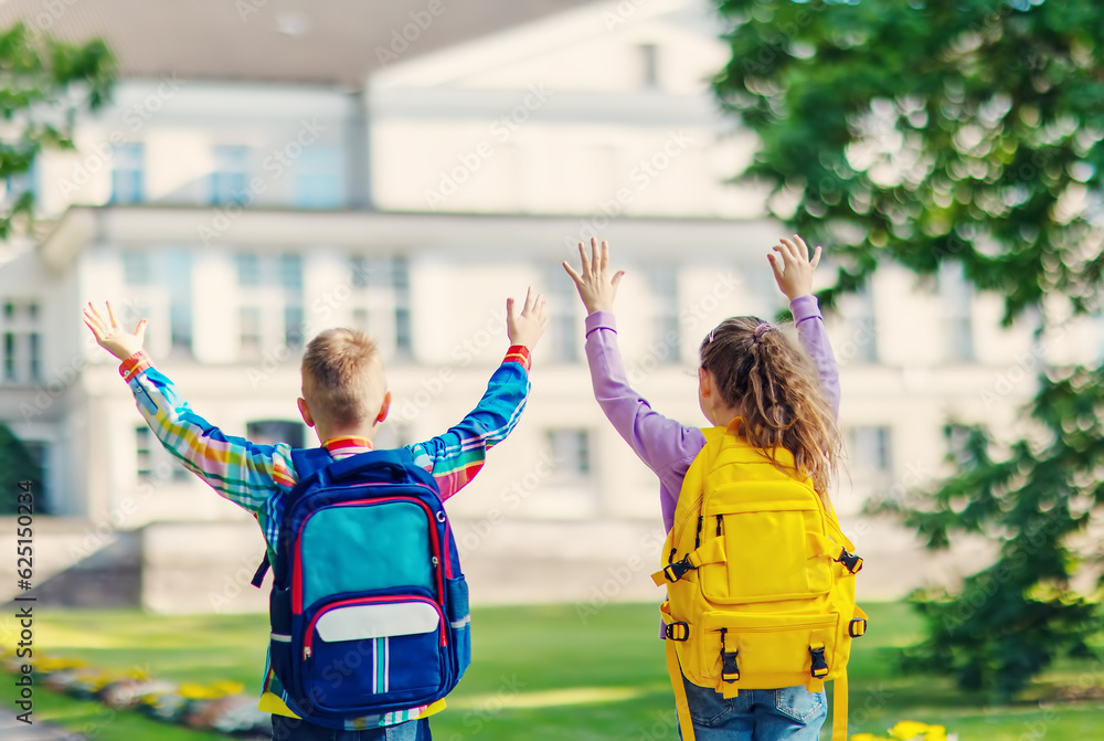 Girl and boy standing with raising hands in the park near the school.