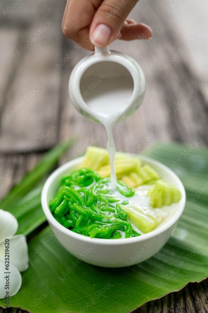 Close up of Appetizing Lod Chong being poured with fresh coconut milk on banana leaf on wooden backg