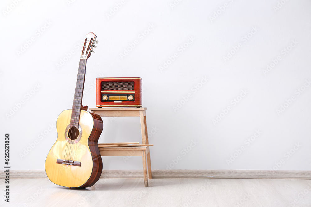 Retro radio receiver and guitar near light wall