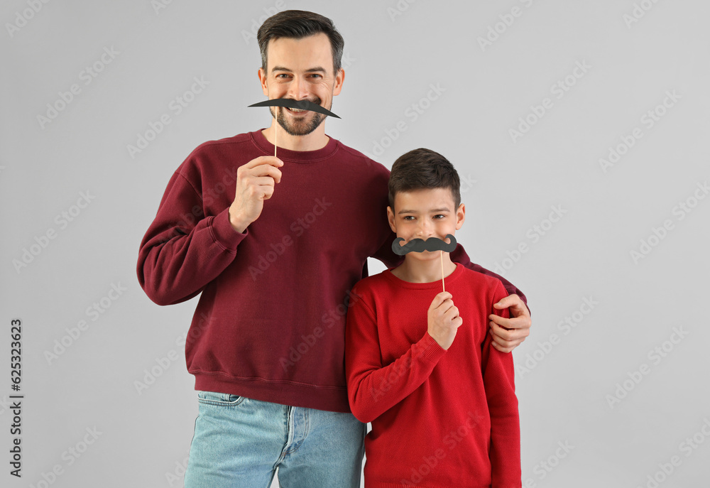 Portrait of father and his little son with paper mustache on light background