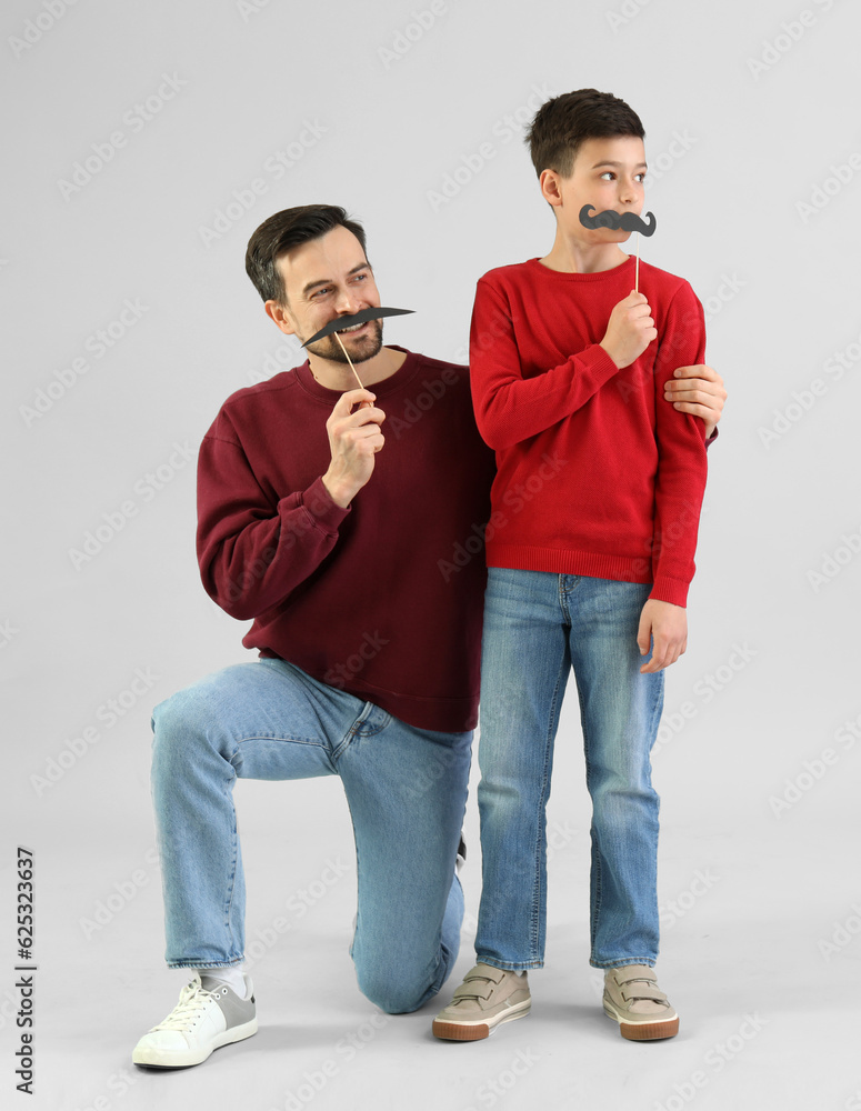 Portrait of father and his little son with paper mustache on light background