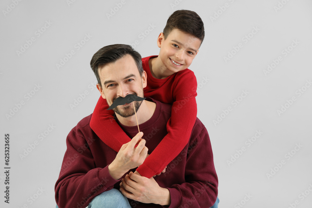 Portrait of father and his little son with paper mustache on light background