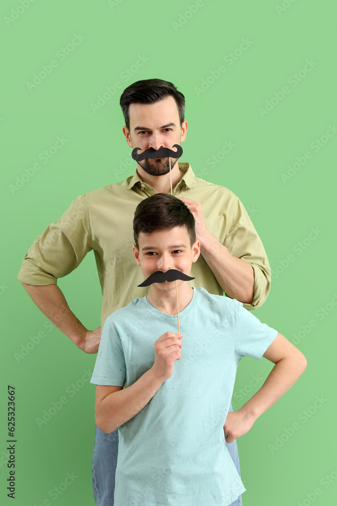 Portrait of father and his little son with paper mustache on green background