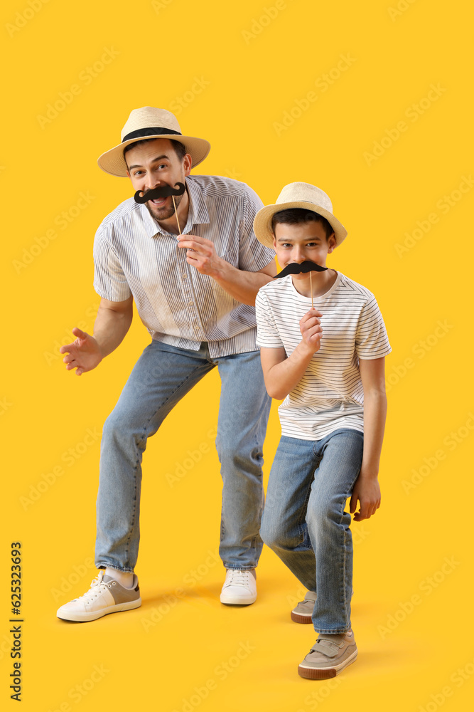 Portrait of funny father and his little son with paper mustache on yellow background