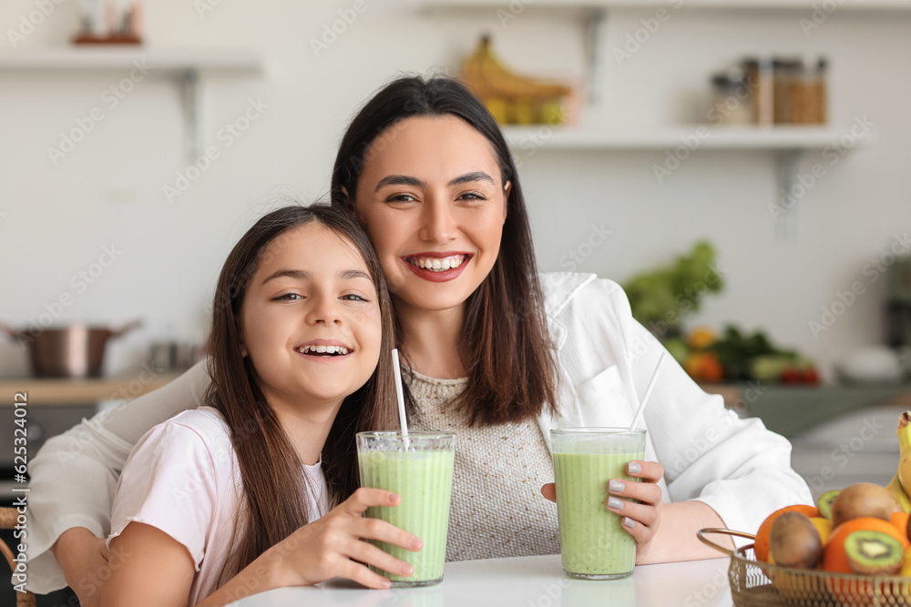 Little girl with her mother drinking green smoothie at table in kitchen