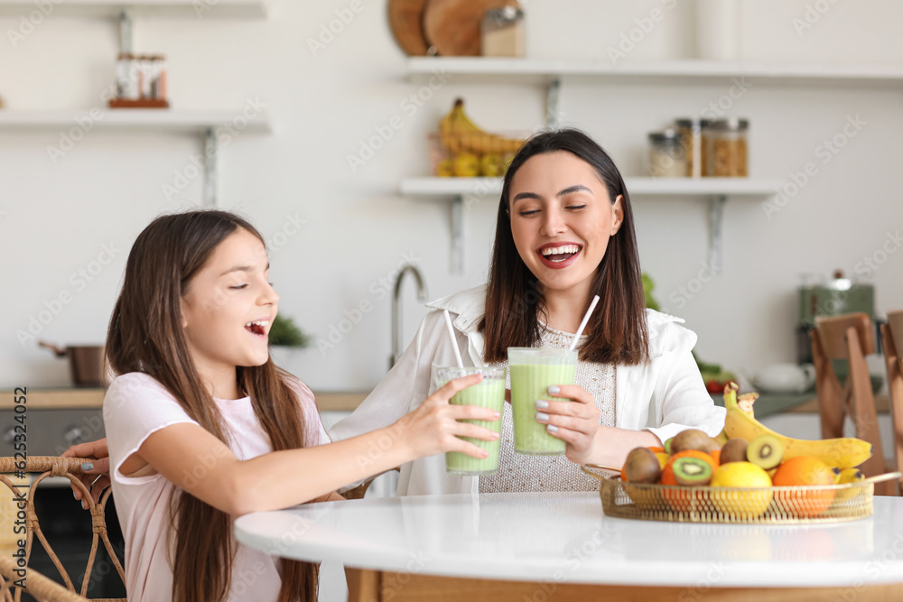 Little girl with her mother drinking green smoothie at table in kitchen