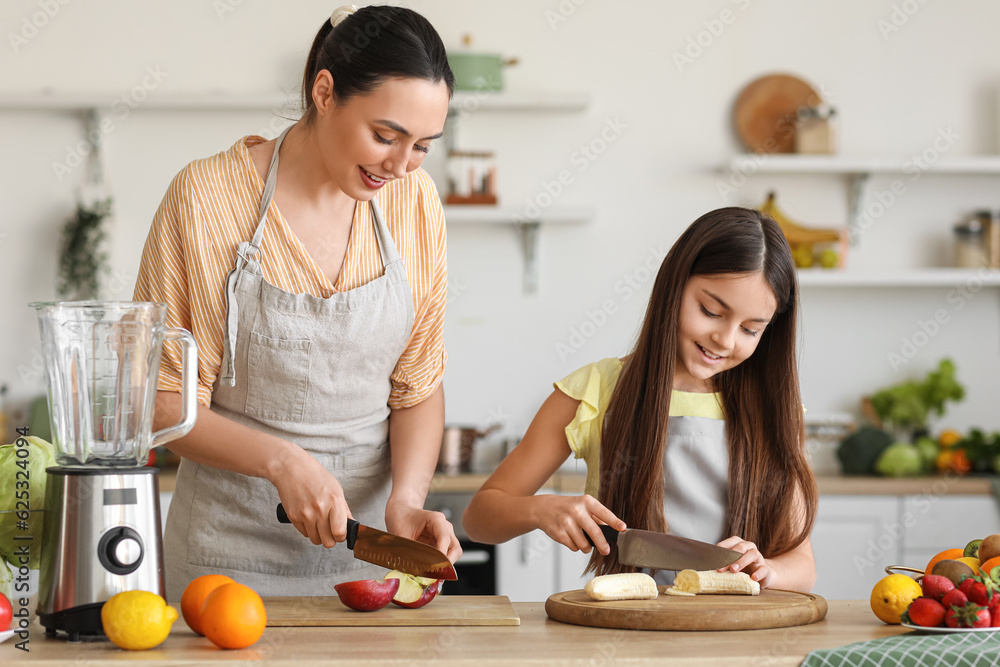 Little girl with her mother cutting fruits for smoothie in kitchen