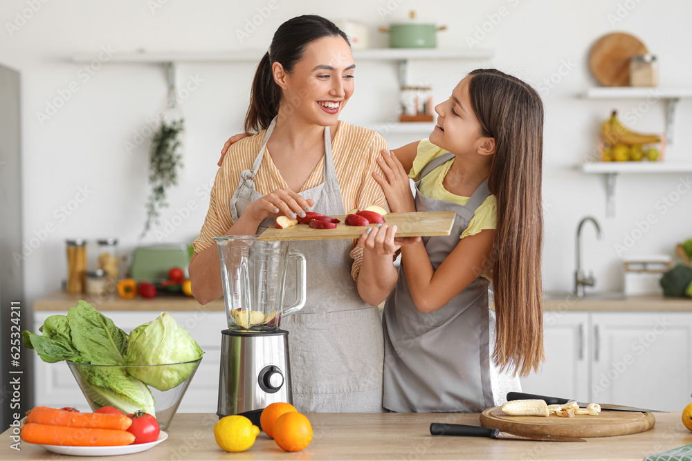 Little girl with her mother putting cut apple into blender in kitchen