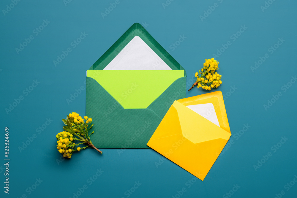 Envelopes with blank cards and blooming plant branches on color background