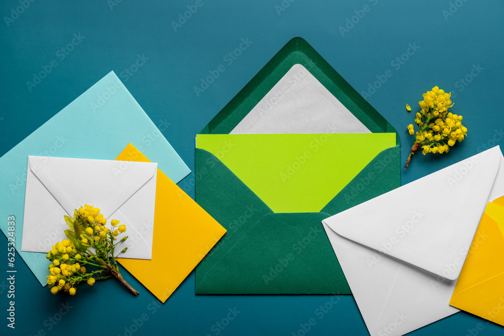 Envelopes with blank card and blooming plant branches on color background, closeup