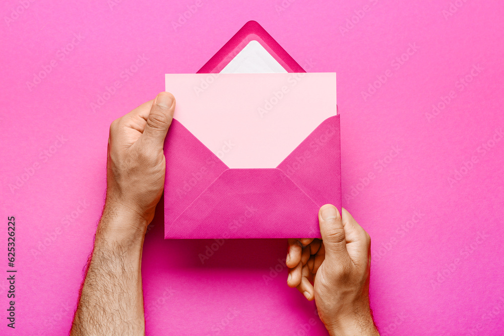 Male hands with envelope and blank card on pink background, closeup