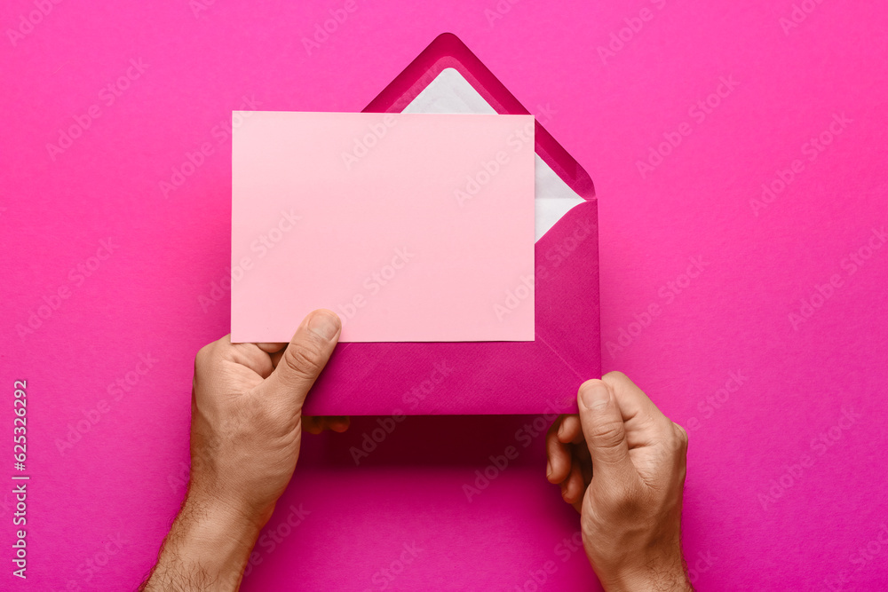 Male hands with envelope and blank card on pink background, closeup