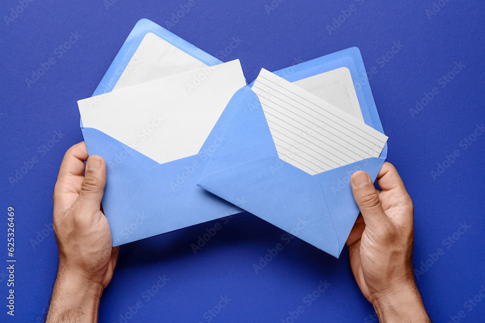 Male hands with envelopes and blank cards on blue background, closeup