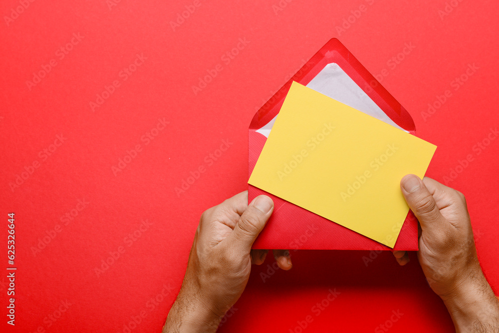 Male hands with envelope and blank card on red background, closeup