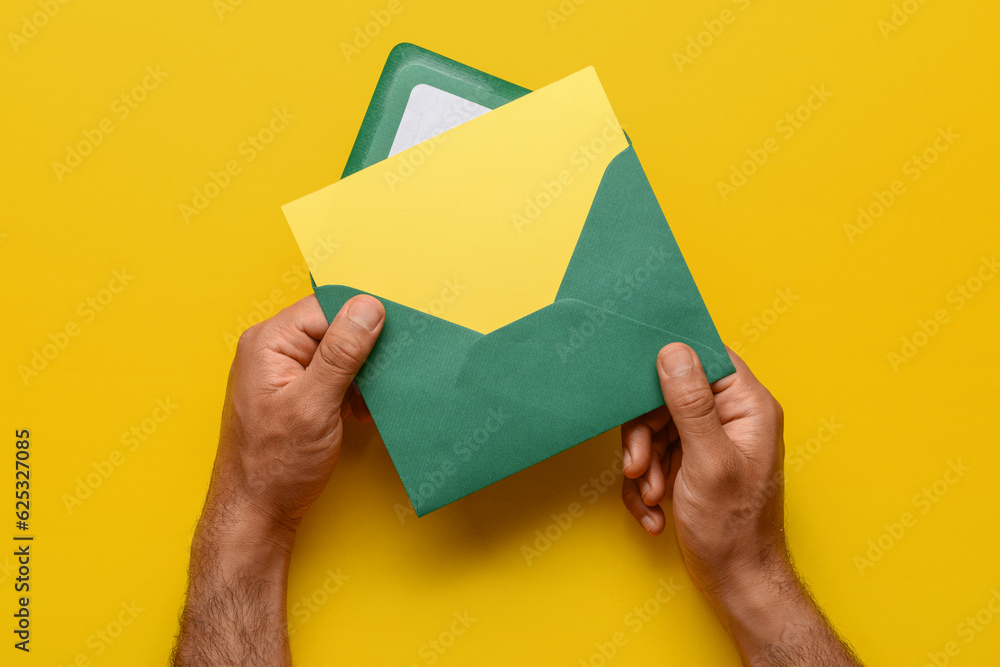 Male hands with envelope and blank card on yellow background, closeup