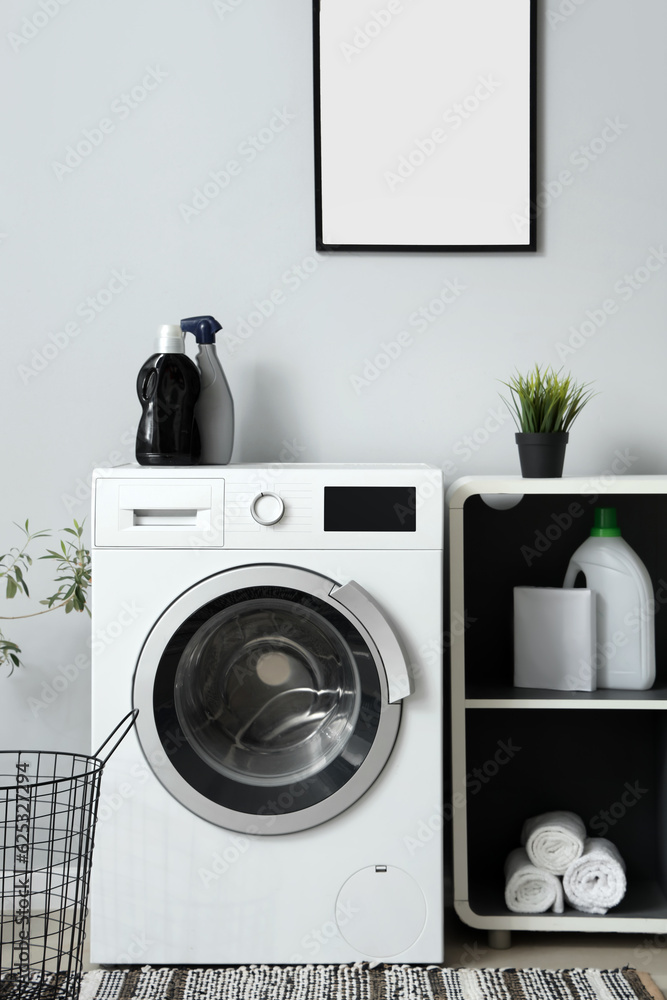 Washing machine and shelving unit with bottles of detergent near grey wall