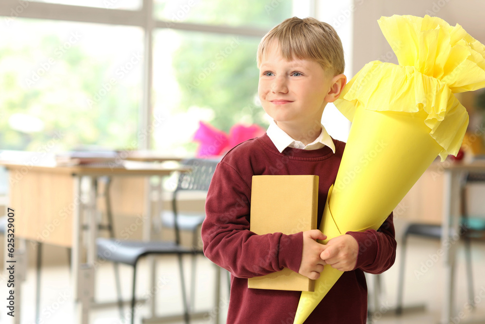 Happy little boy with yellow school cone and book in classroom