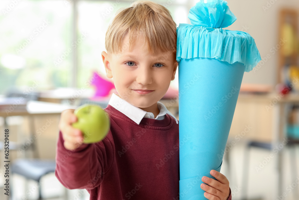 Happy little boy with blue school cone and fresh apple in classroom