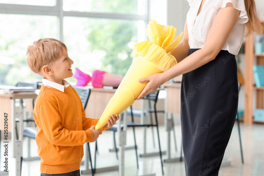 Happy little boy with yellow school cone and teacher in classroom