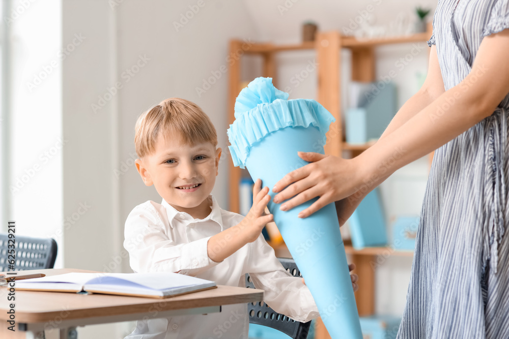 Teacher greeting her happy pupil with blue school cone in classroom