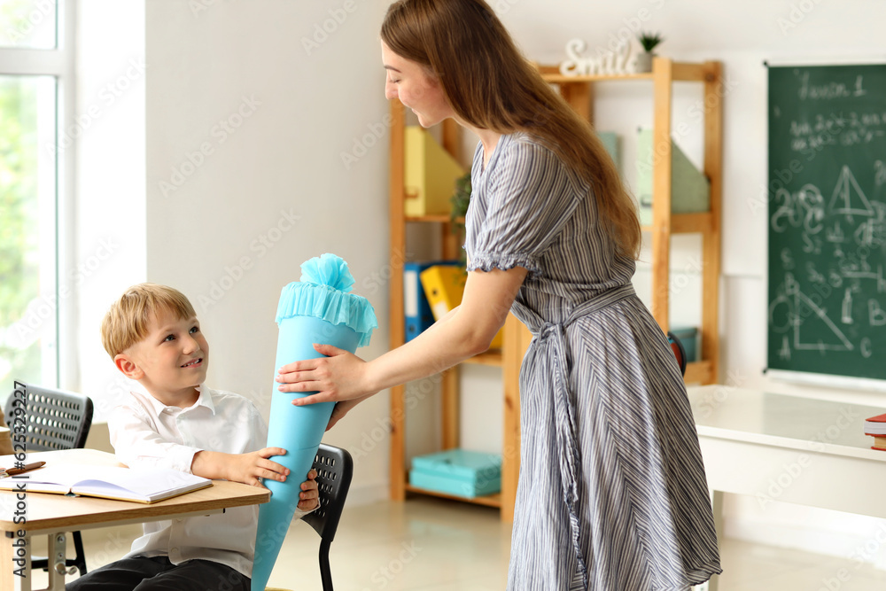 Teacher greeting her happy pupil with blue school cone in classroom