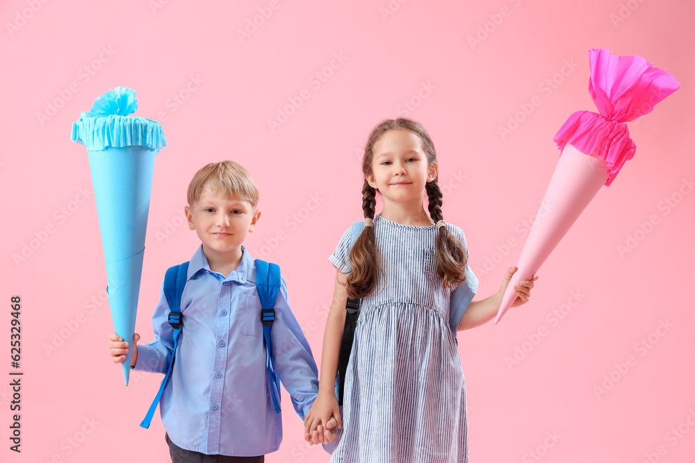 Happy little classmates with backpacks and colorful school cones on pink background