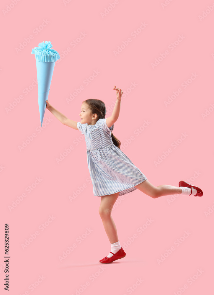 Happy little girl with blue school cone jumping on pink background