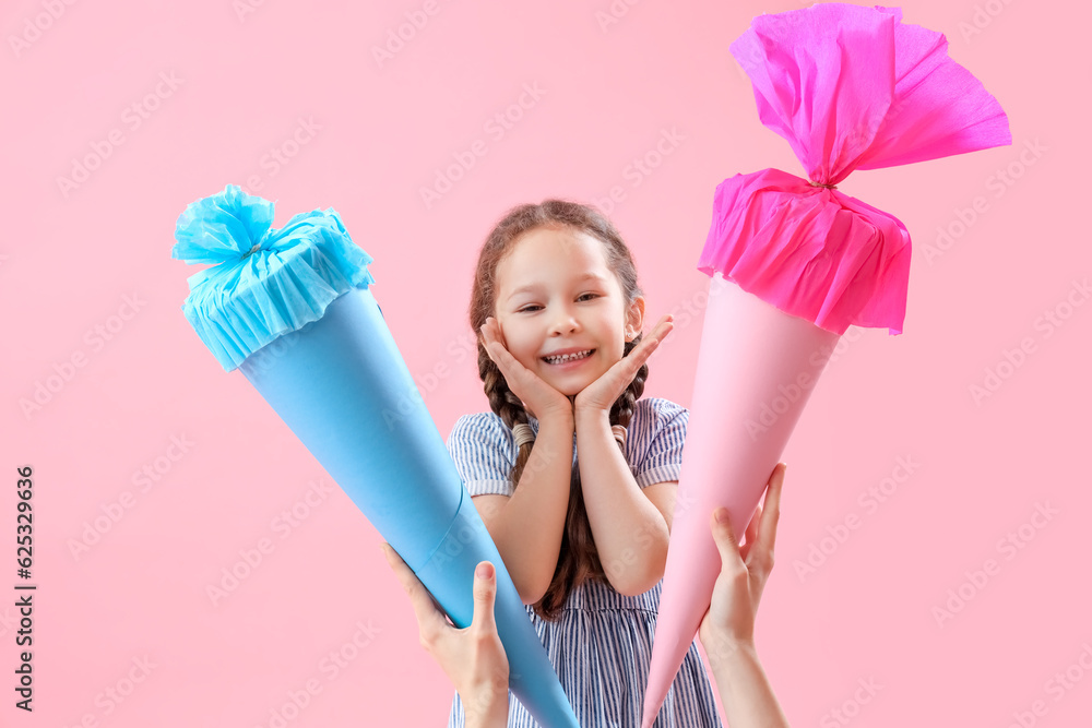 Mother greeting her happy daughter with colorful school cones on pink background