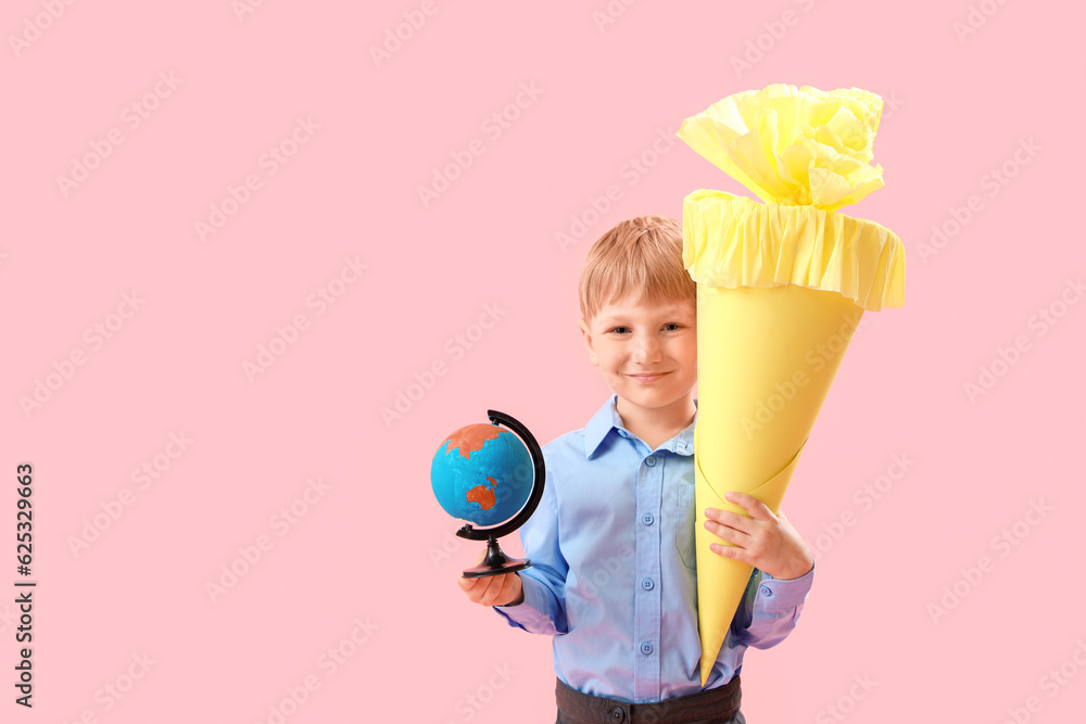 Happy little boy with yellow school cone and globe on pink background