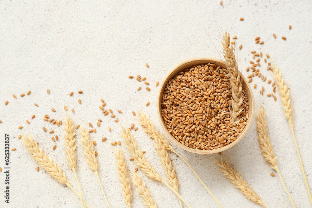 Wooden bowl with wheat ears and grains on white table